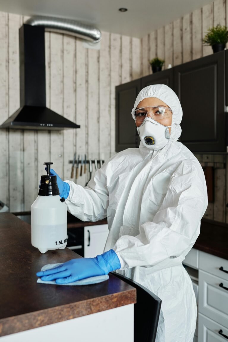 Female disinfection specialist in protective gear cleaning a kitchen indoors.